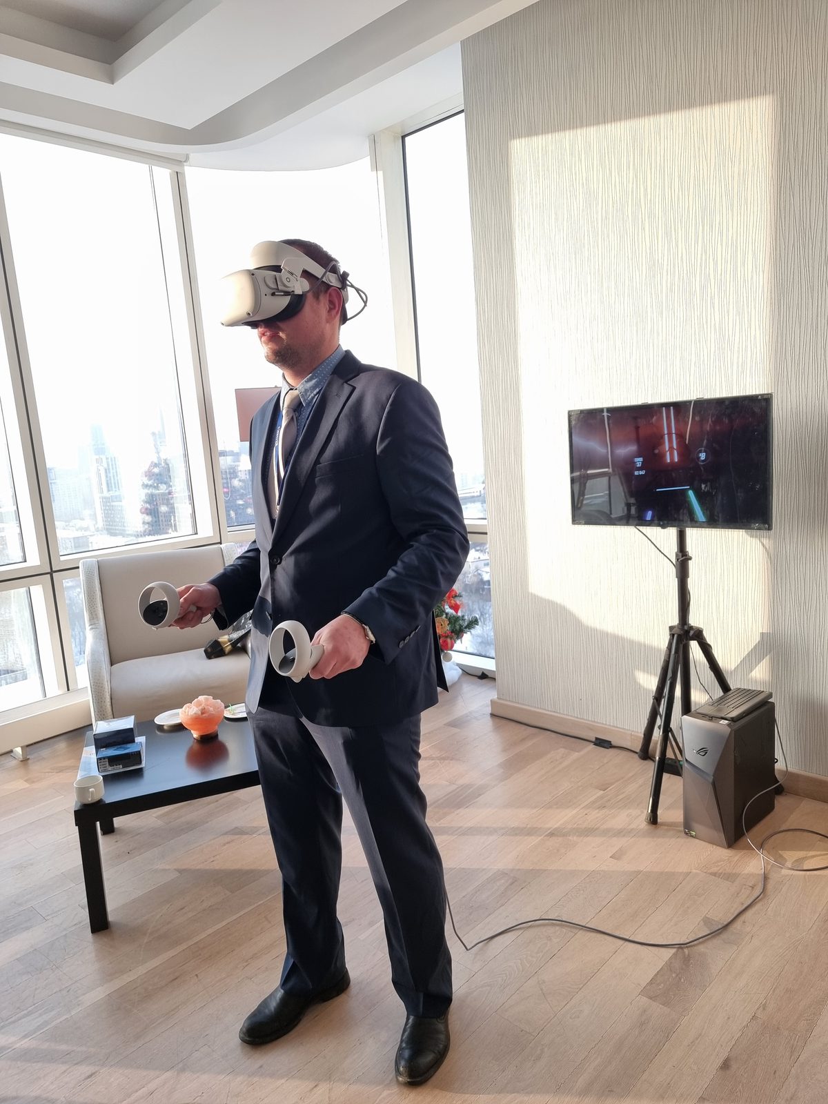 Гость в костюме играет в VR в переговорной, рядом ПК-станция и экран