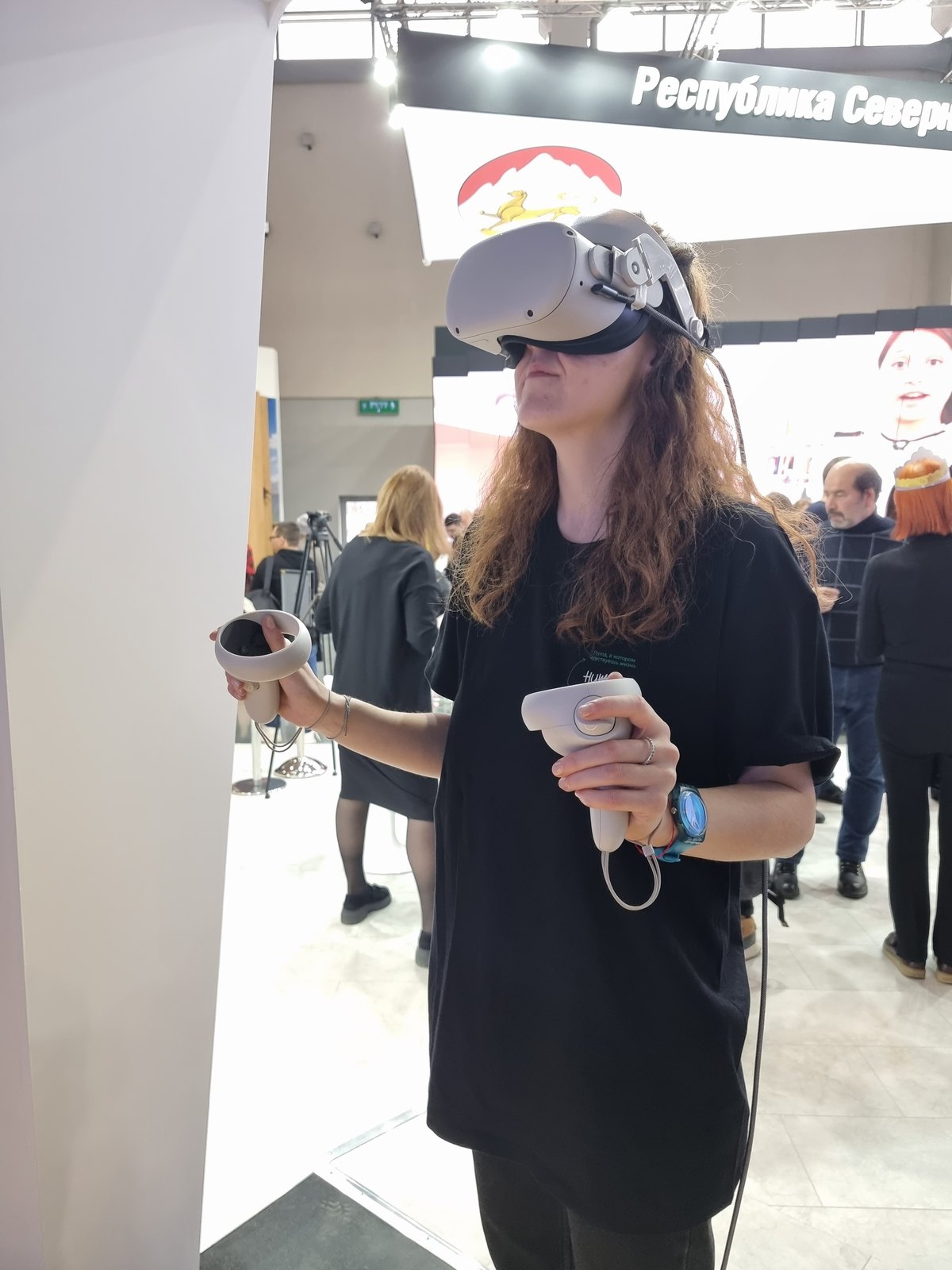 Посетительница в VR-шлеме с контроллерами на стенде выставки